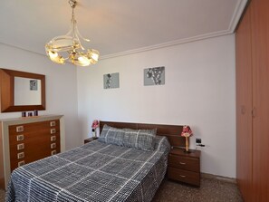 Une chambre à coucher comprenant un lit, une commode, une table de chevet, une lampe et un luminaire au plafond.