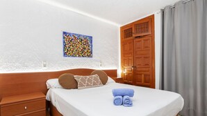 Una camera d'hotel con un letto rifatto, un comodino in legno, un piccolo cassetto, un'opera d'arte appesa al muro e un armadio in legno.