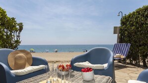 Un'area relax in spiaggia con mobili in vimini, un vassoio con bicchieri e frutta, e vista sul mare.