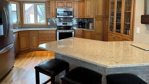 Una cocina con armarios de madera, encimera de granito, refrigerador de acero inoxidable, microondas y cafetera.