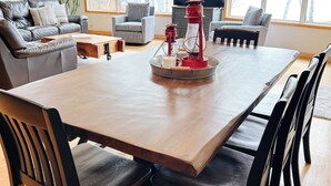 Un salón amplio con una gran mesa de comedor de madera, sillas de madera oscura, un sofá gris y un televisor.