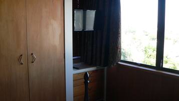 A room with a wooden wardrobe, a desk with a chair, and a window with curtains.