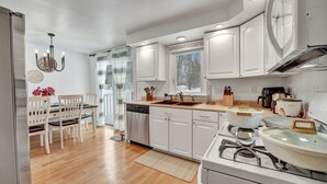 Une cuisine moderne avec des meubles blancs, une cuisinière à gaz et un coin repas agrémenté de chaises en bois et d’un lustre.