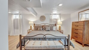 Une chambre à coucher avec un grand lit, des tables de chevet, un banc et une commode en bois.