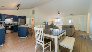Une cuisine spacieuse avec des meubles de couleur bleu foncé, un réfrigérateur en acier inoxydable et un coin repas comprenant une table en bois et des chaises blanches.