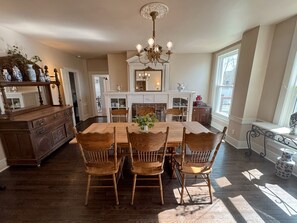 A dining area with a wooden table and chairs, a chandelier, and a fireplace. - The Gibson Grand (North East)