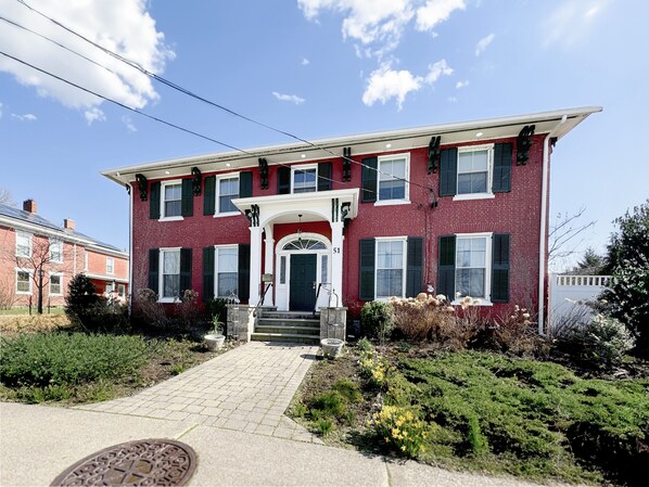 A two-story red brick house with a white porch and green shutters. - The Gibson Grand (North East)