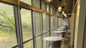 A row of round tables with grey upholstered chairs, large windows with metal frames, and hanging pendant lights. - yamanoyu (Kirishima)