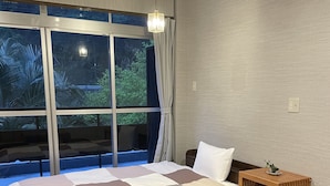 A modern bedroom with a large bed, a wooden nightstand, a small table with a plant, and a view of greenery outside. - yamanoyu (Kirishima)