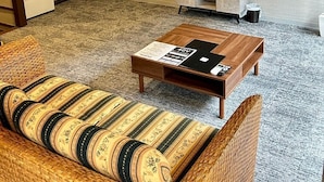 A modern living room with a sofa, a coffee table, a flat-screen TV mounted on the wall, a small cabinet, and a plant. - yamanoyu (Kirishima)