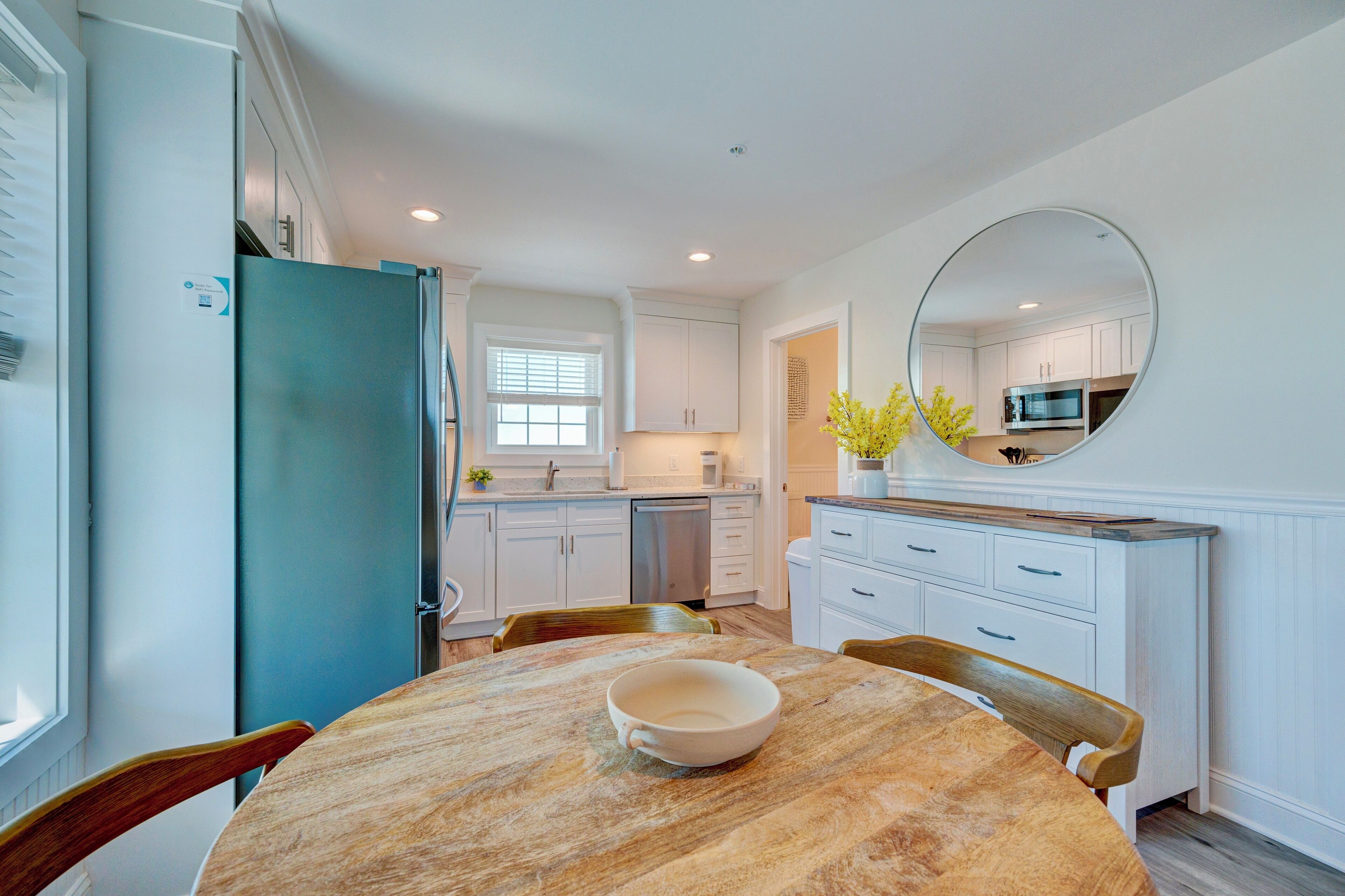 A modern kitchen with white cabinets, a blue refrigerator, and a dining area with a wooden table and chairs.