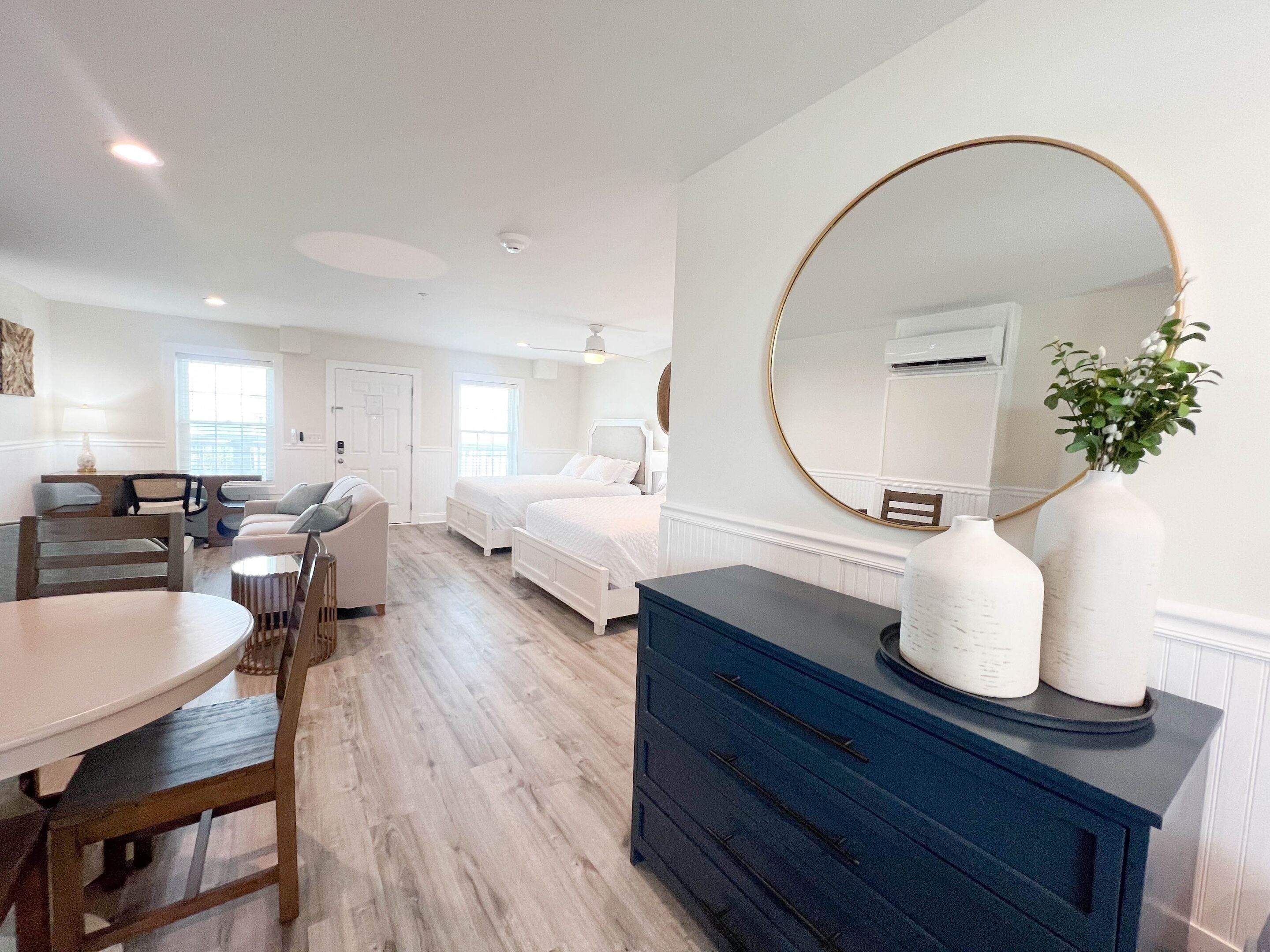 A spacious room with a large bed, a dining area with a table and chairs, and a blue dresser with vases.