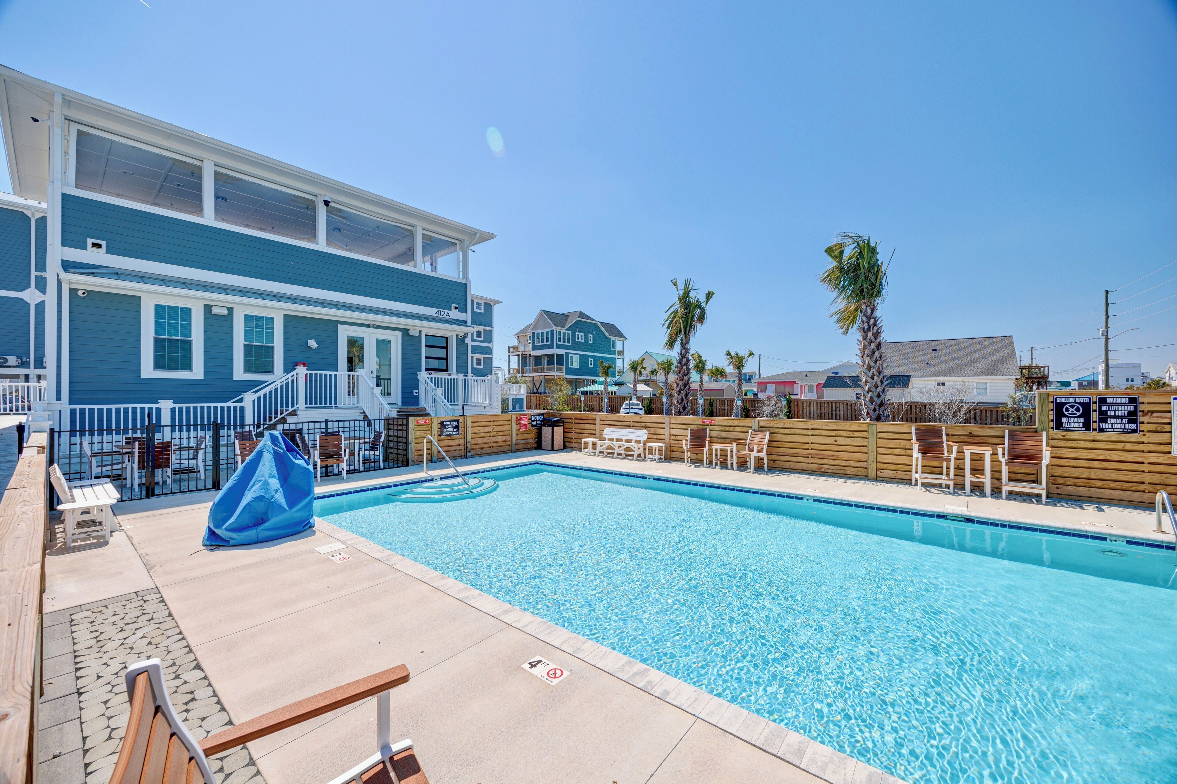 A pool area with a wooden deck, lounge chairs, and a covered seating area.