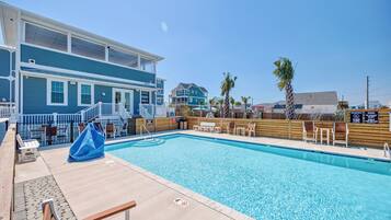 A pool area with a wooden deck, lounge chairs, and a covered seating area.
