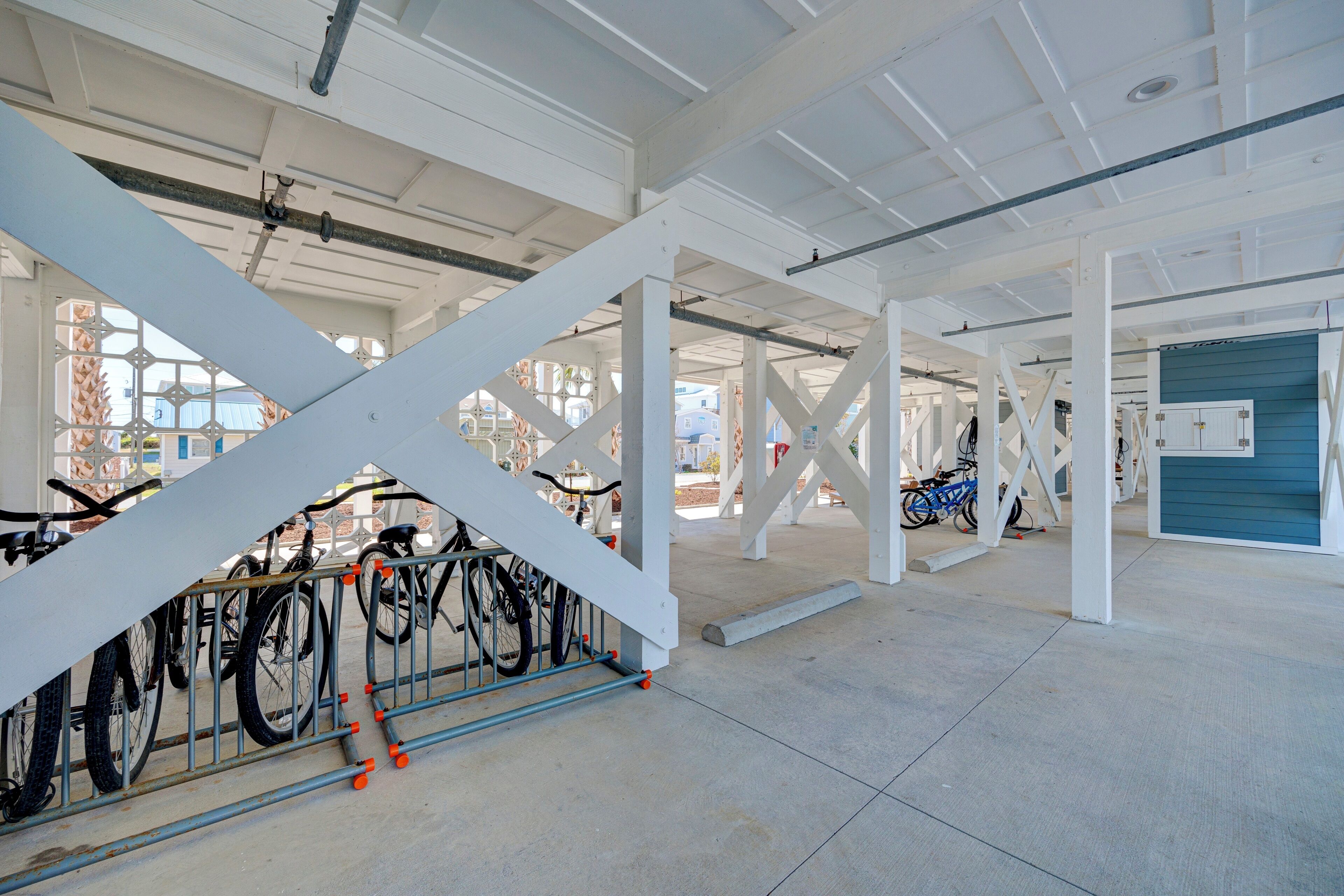 A spacious indoor area with white structural beams and a concrete floor, featuring a bicycle rack with several bicycles.