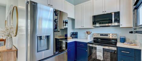 A modern kitchen with stainless steel appliances, blue cabinets, and a wooden sideboard.