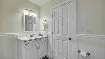 A bathroom with a white vanity, a mirror with lights, a door, and a towel rack.