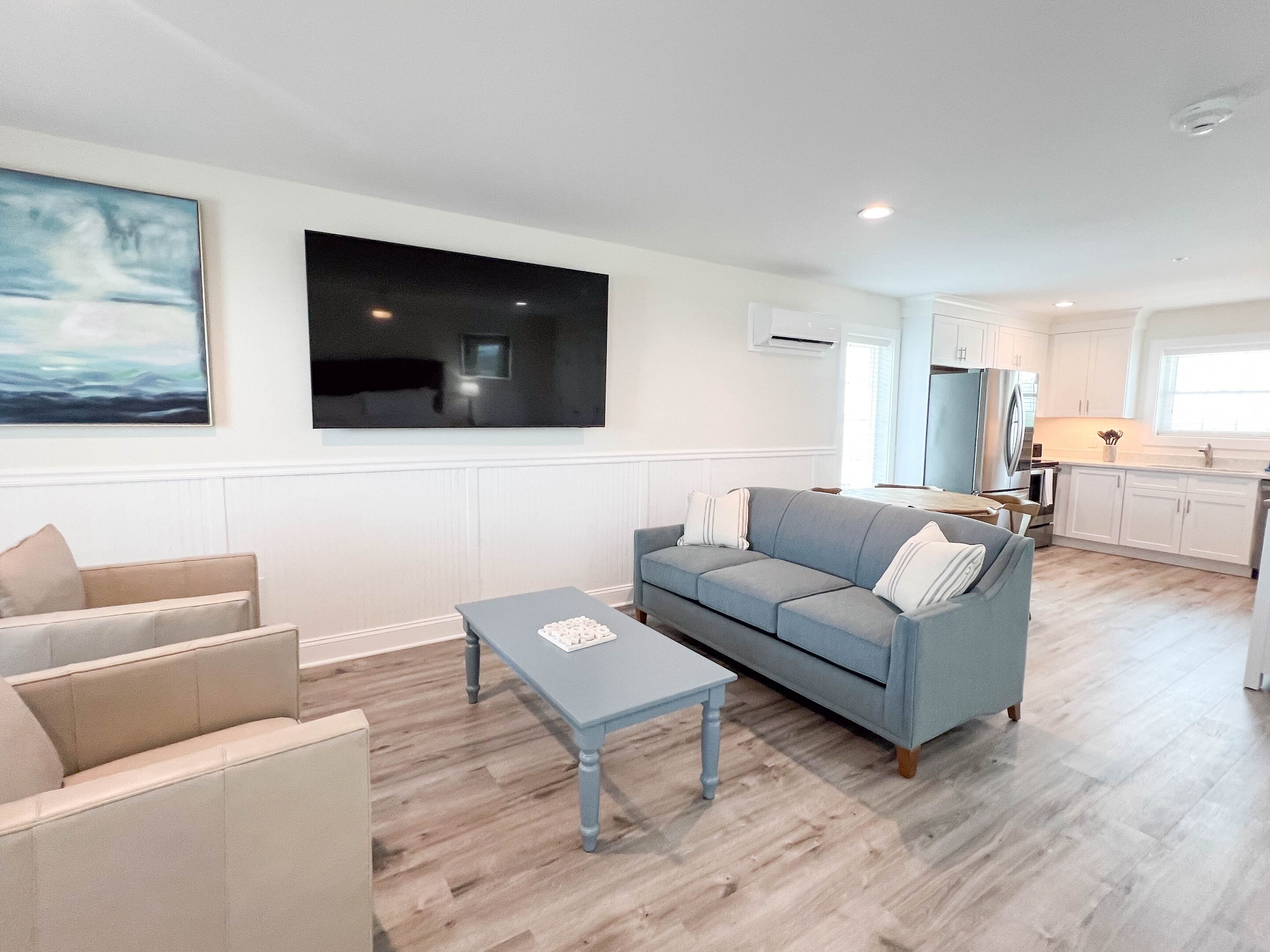 A modern living room with a grey sofa, a small table, and a large flat-screen TV mounted on the wall.