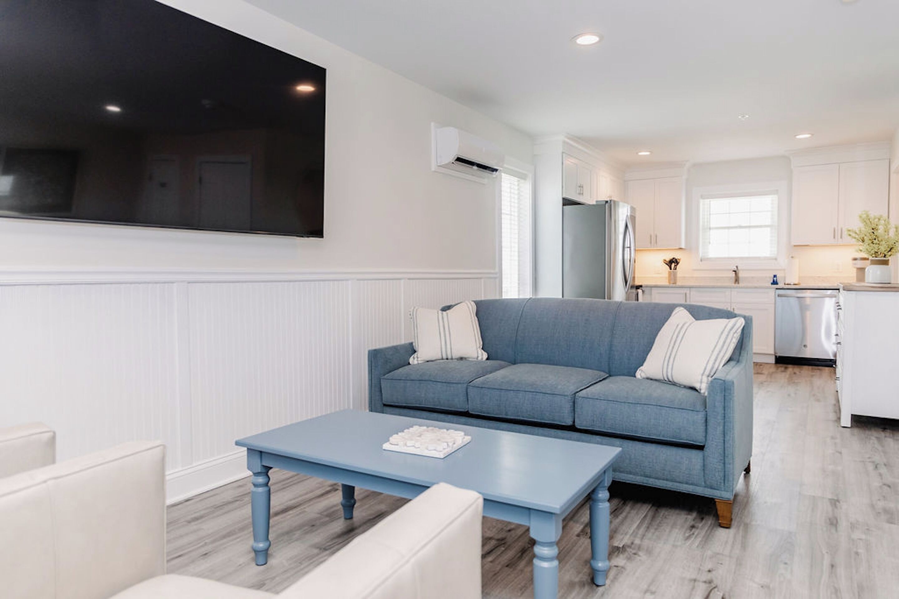 A modern living room with a blue sofa, a white coffee table, and a flat-screen TV mounted on the wall.