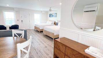 A modern hotel room with a wooden floor, a round mirror, a wooden dresser, a bed, a desk, and a chair.