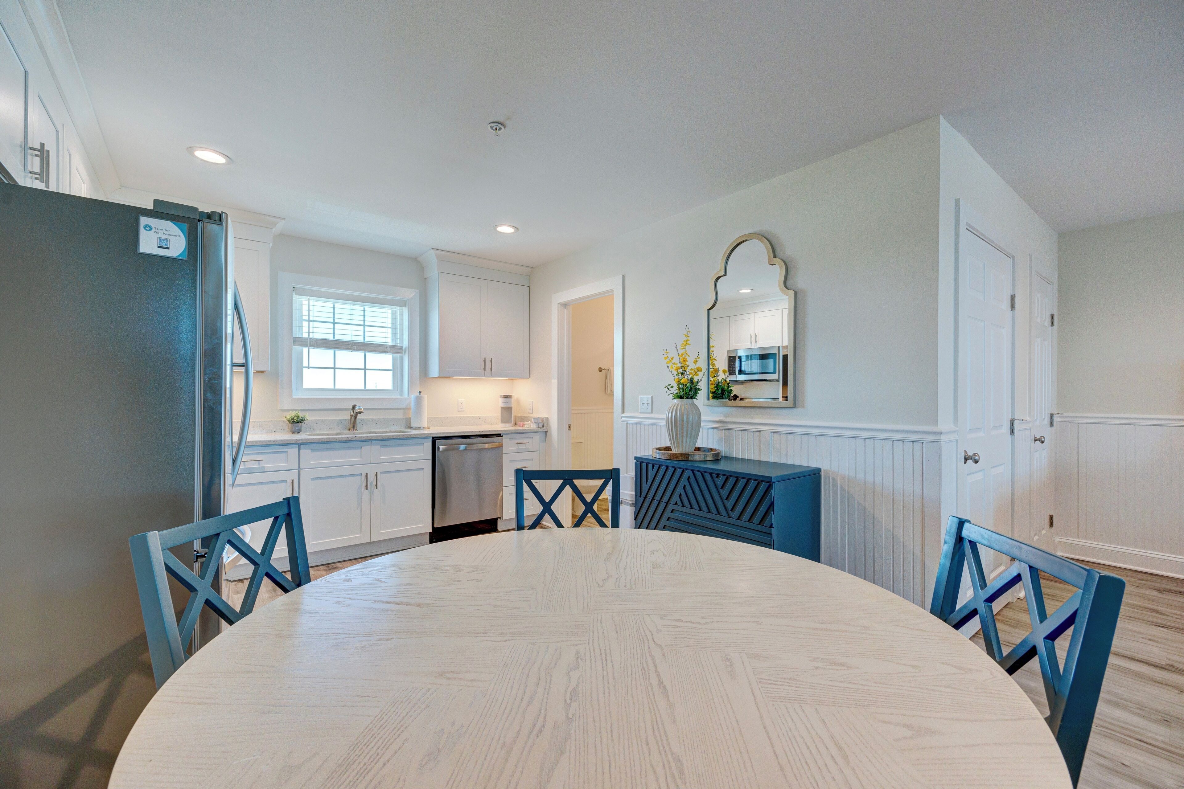 A modern kitchen with white cabinets, a stainless steel refrigerator, and a blue dining table with matching chairs.