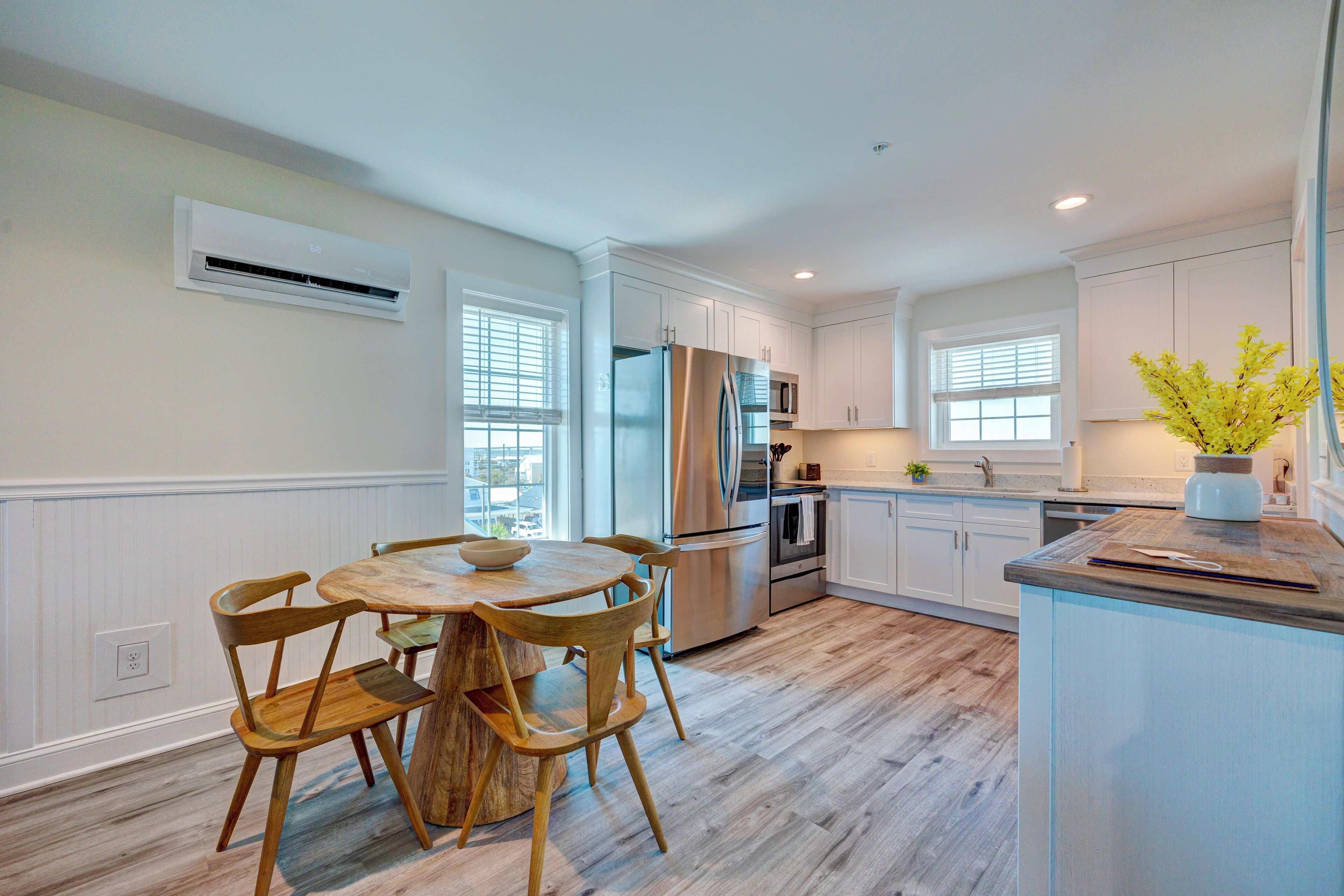 A modern kitchen with white cabinetry, a stainless steel refrigerator, and a wooden dining table with chairs.