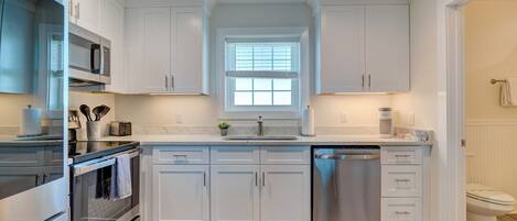 A modern kitchen with white cabinets, stainless steel appliances, and a window above the sink.