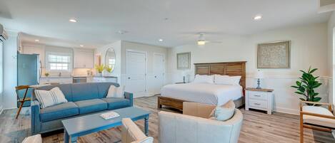A spacious living area with a sofa, armchair, and coffee table, a bedroom with a large bed and nightstands, and a kitchen area with cabinets and a refrigerator.