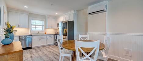 A modern kitchen with white cabinetry, a wooden dining table, and a built-in oven.