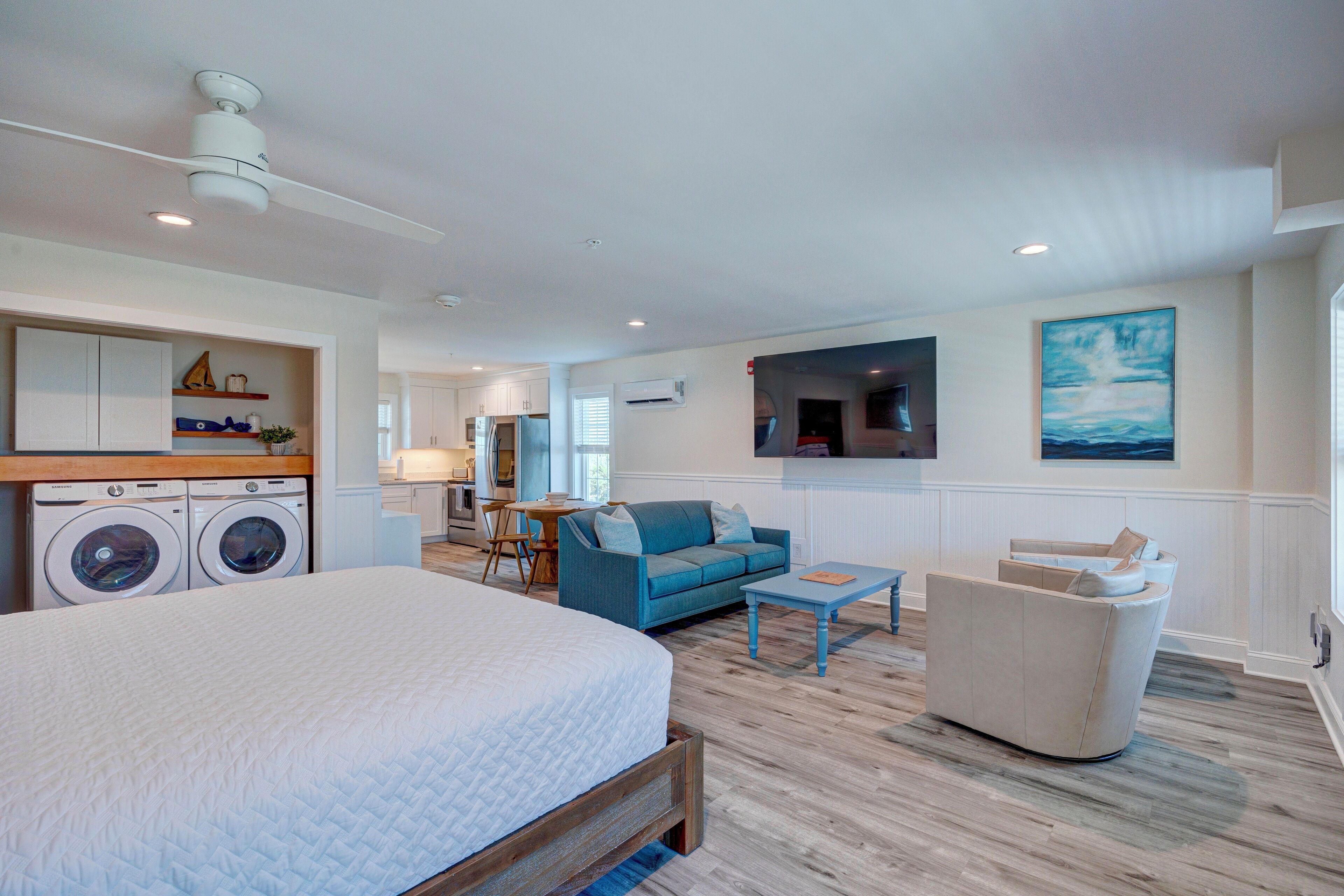 A bedroom with a large bed, a washing machine, a blue sofa, and a small table.