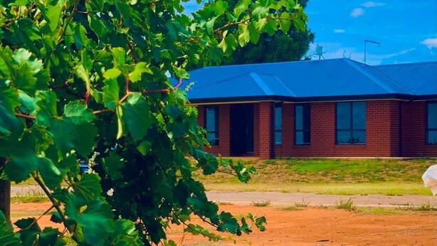 Un edificio con facciata in mattoni rossi e tetto blu, circondato da terreno sterrato e vegetazione.