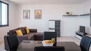 Ein modernes Wohnzimmer mit einer Couch, einem Esstisch mit Stühlen, einem Fernseher und zwei gerahmten Bildern an der Wand.