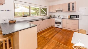 A modern kitchen with wooden flooring, a central island, and a view of greenery outside. - Sandscape (Sandy Point)