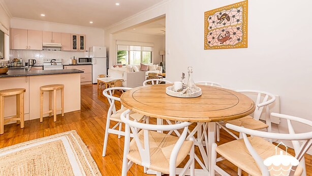 A spacious kitchen with a central island, white cabinetry, and a dining area with a wooden table and white chairs. - Sandscape (Sandy Point)