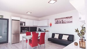 Una cocina moderna con armarios blancos, un refrigerador de acero inoxidable y una zona de comedor con sillas rojas.