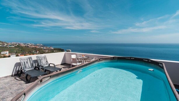 Una piscina infinita en la azotea con sillones de descanso y vistas al océano.