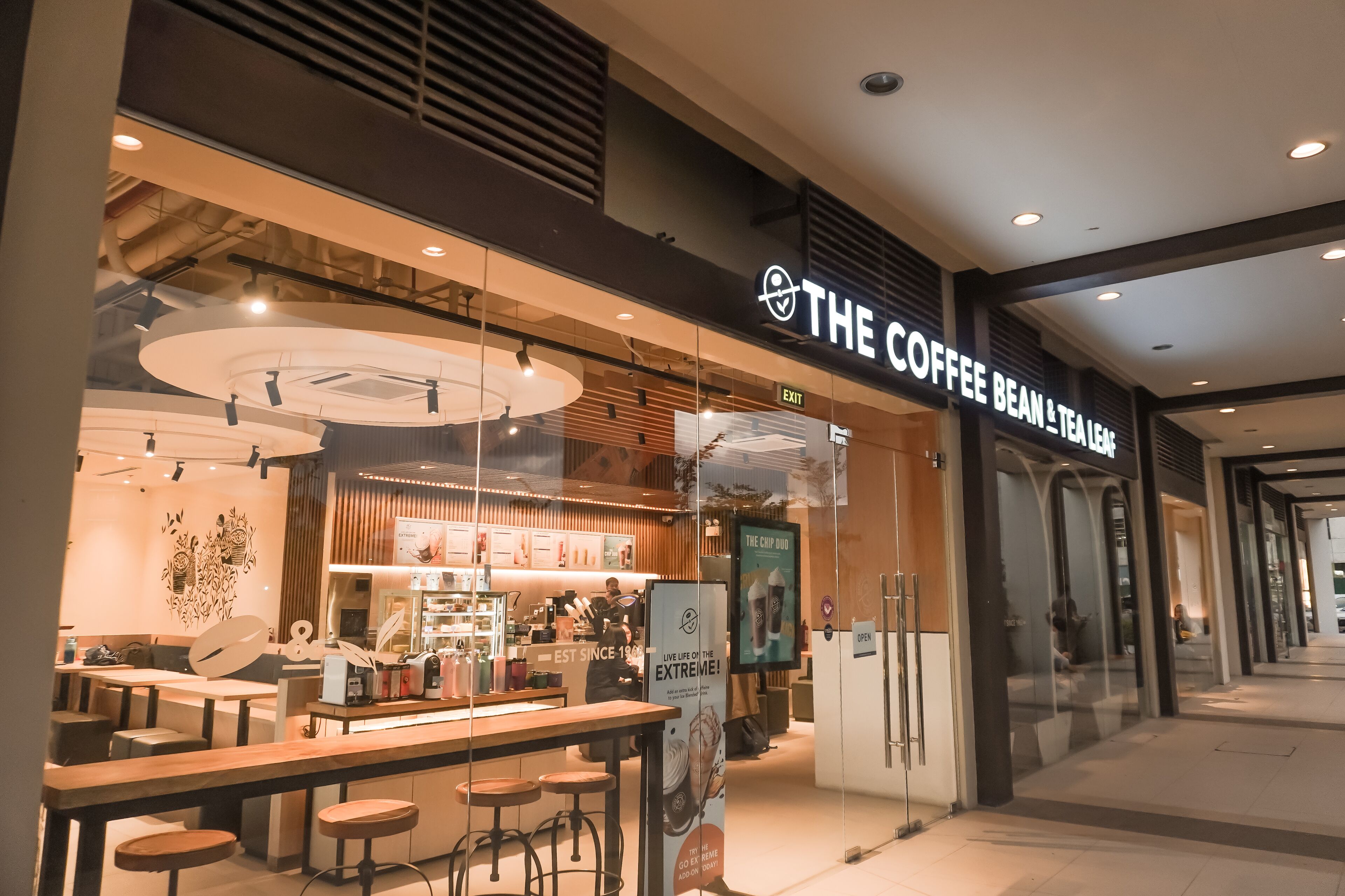 A coffee shop with a modern interior, including a counter and stools, and a sign reading "The Coffee Bean & Tea Leaf".
