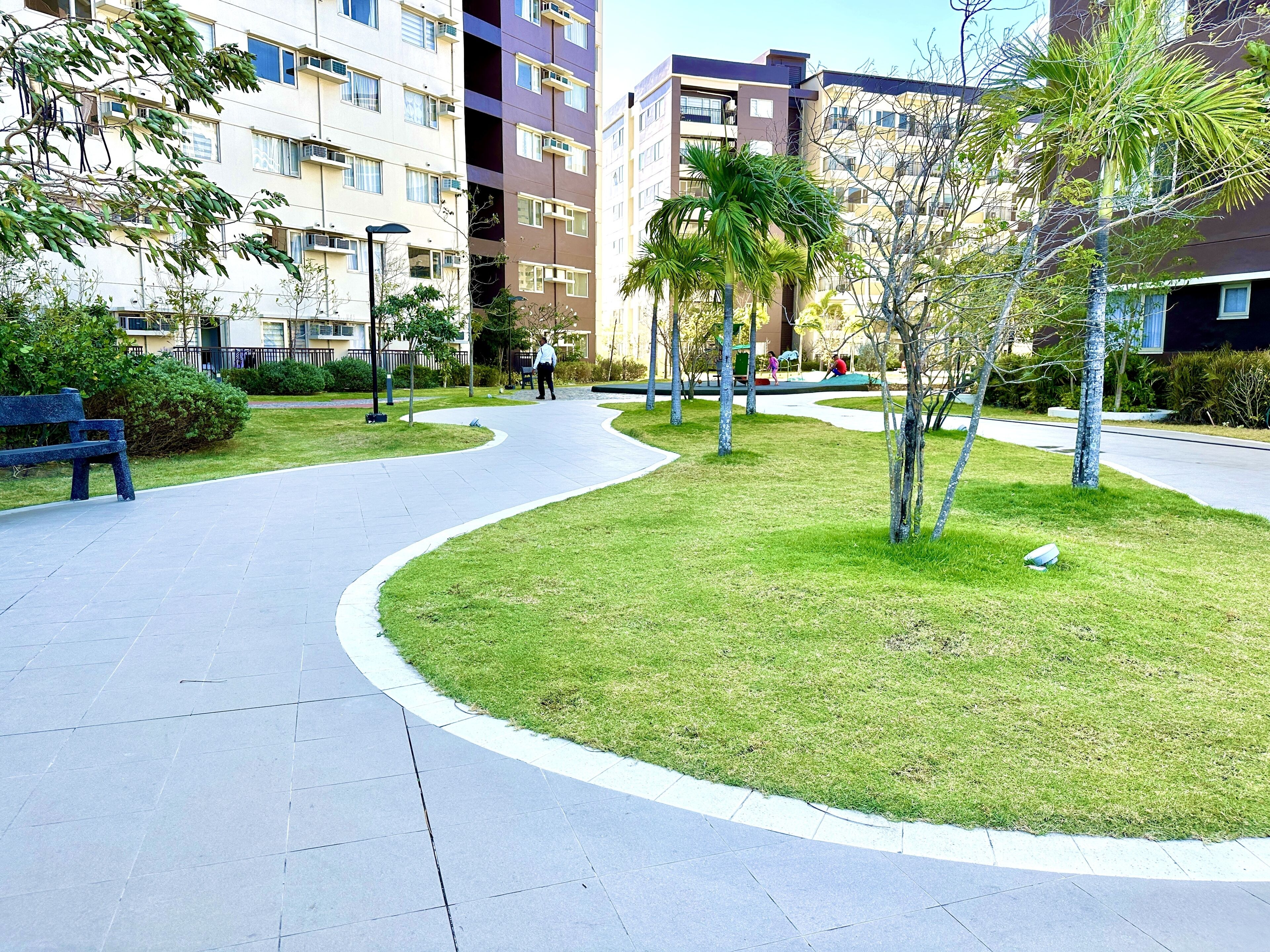 A residential area with a curved pathway, benches, and young trees.