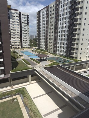 A high-rise residential building with multiple balconies, a swimming pool, and a landscaped courtyard.