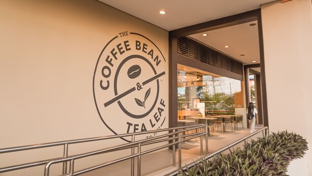 A coffee shop entrance with a large logo on the wall and outdoor seating visible through the glass. - Stay comfy & feel Homealike 32 (Iloilo)