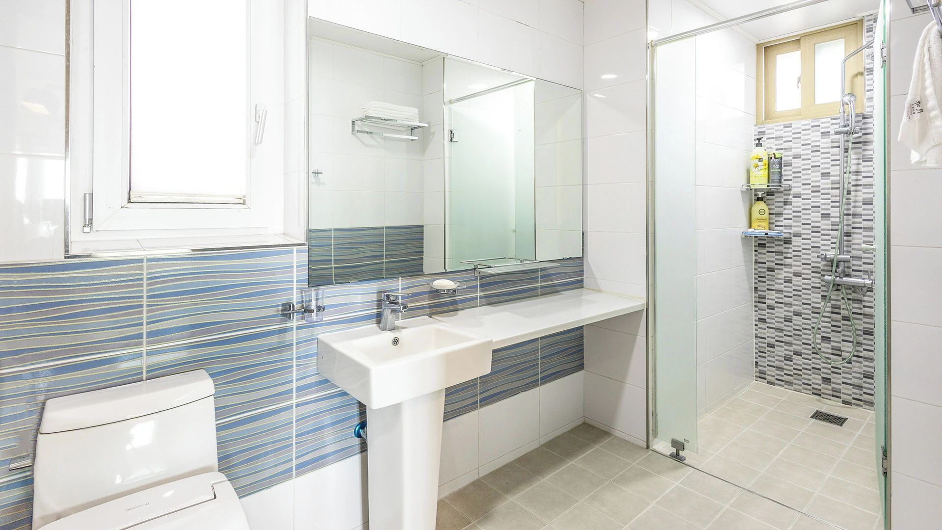 A modern bathroom with a glass shower enclosure, a white sink, and a striped tile backsplash.
