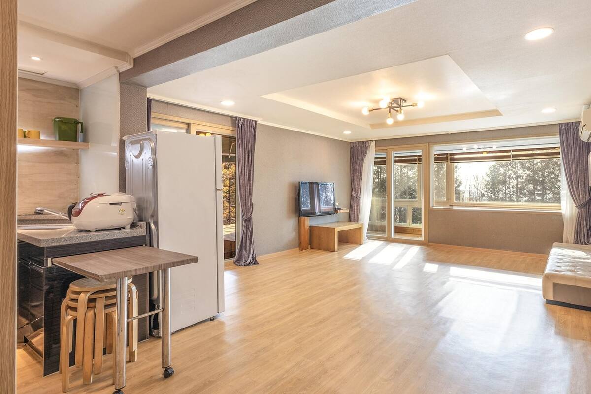 Eine moderne Küche mit integriertem Backofen, einer Kaffeemaschine und einem Spülbecken. Es ist ein Holzesstisch mit einer Bank und ein an der Wand befestigtes Fernsehgerät vorhanden.