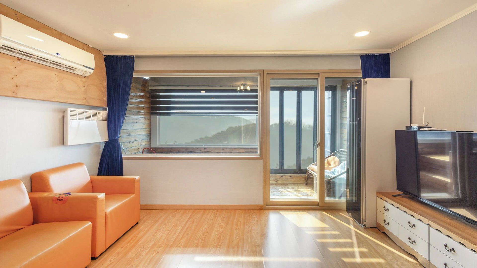 A modern living room with a sofa, a television, and a sliding glass door leading to a balcony.