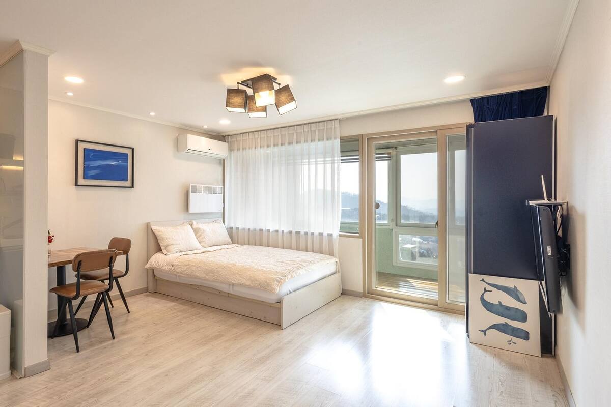 Ein modernes Hotelzimmer mit Bett, Schreibtisch, Stuhl, Küchenzeile und einem Balkon mit Stadtblick.
