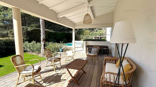 Eine überdachte Terrasse im Freien mit Korbmöbeln, einer gepolsterten Bank und einem Tisch.