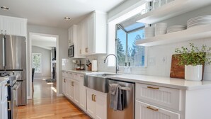 Une cuisine moderne avec des meubles blancs, des appareils en acier inoxydable et un plancher en bois.