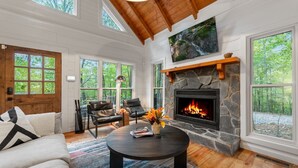 A spacious living room with a stone fireplace, large windows, and a cozy seating area. - Modern Log Cabin - Hot Tub, Fire Pit, Spa-like bathroom in secluded nature haven (Blue Ridge)