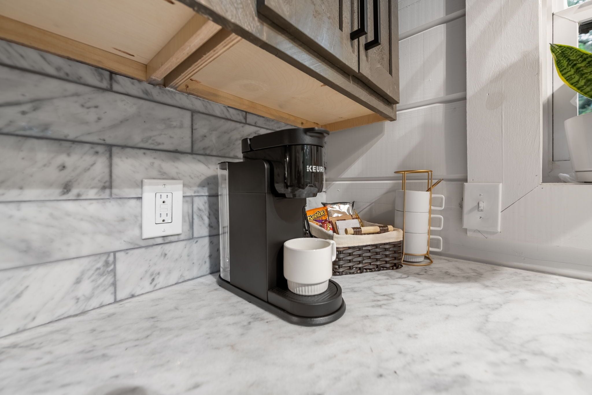 A modern kitchen with a built-in coffee machine, a marble backsplash, and a basket with snacks.