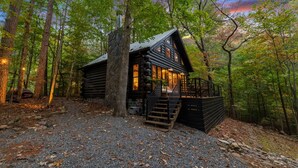 A log cabin with a stone chimney, surrounded by a forest. - Modern Log Cabin - Hot Tub, Fire Pit, Spa-like bathroom in secluded nature haven (Blue Ridge)