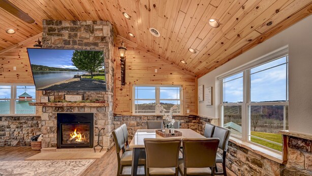 Una habitación acogedora con chimenea de piedra, una mesa de comedor con sillas y ventanas amplias que dan al exterior.
